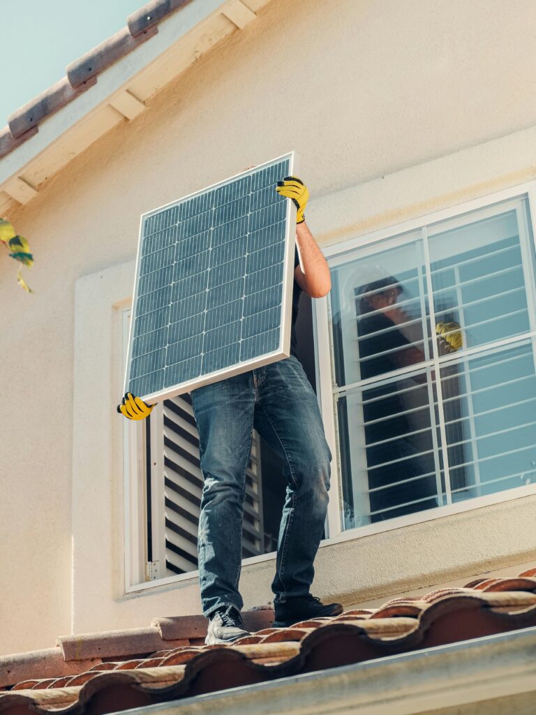Technician carrying a solar panel on a rooftop for installation, promoting renewable energy.
