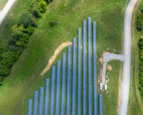 Aerial view showing a solar panel array in a lush rural landscape with a road.