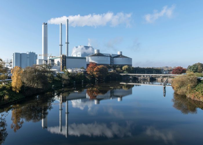 Power plant with smokestacks reflected on a calm river in Hamburg, Germany.