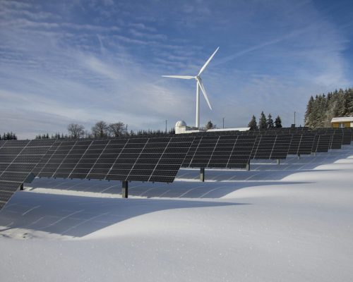Solar panels and wind turbine in a snowy landscape, showcasing renewable energy sources.